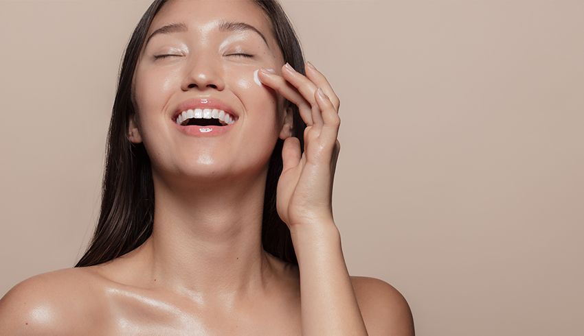 A woman applying lotion to her cheek with one hand